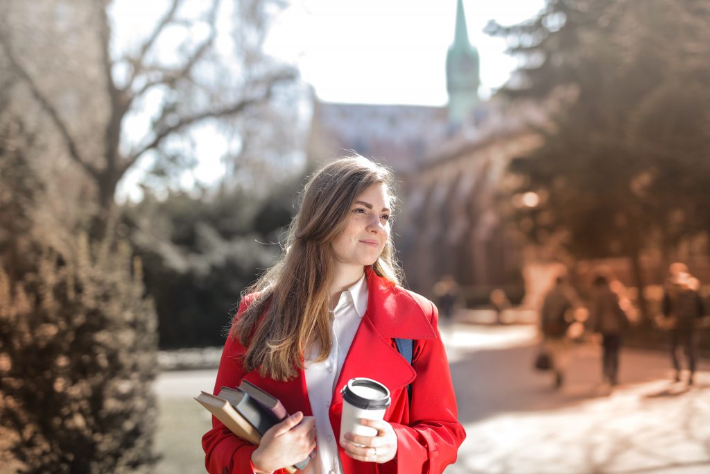 Canva-Woman-in-Red-Coat-Holding-Notebooks-and-Coffee-cup